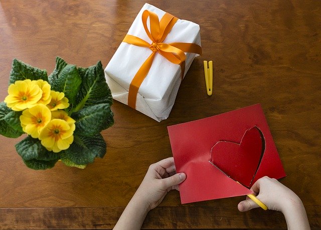 Child's hand cutting out a heart to go with a gift